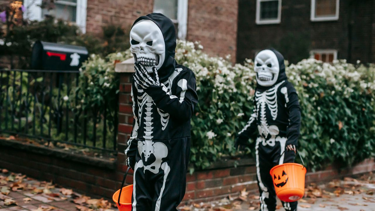 Two children in skeleton costumes trick-or-treating with buckets.