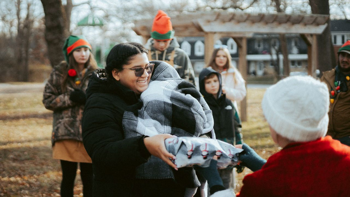 Smiling woman receives wrapped gift outdoors.