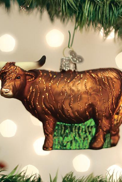 Brown glass Highland cow Christmas ornament with glittery fur texture and long horns hanging on a pine tree.