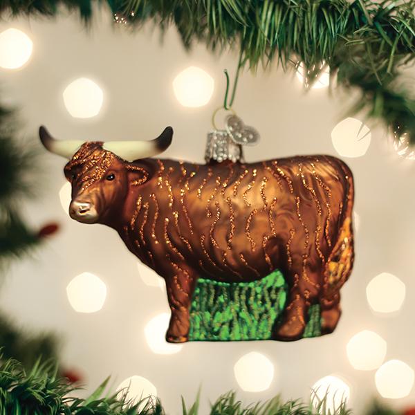 Brown glass Highland cow Christmas ornament with glittery fur texture and long horns hanging on a pine tree.