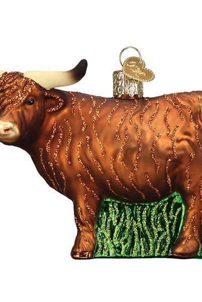 Brown glass Highland cow Christmas ornament with long horns, glittery fur texture, and a green grass base.