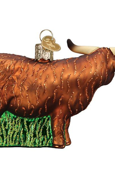 Brown glass Highland cow Christmas ornament with glittery fur texture, long horns, and a green base on a white background.