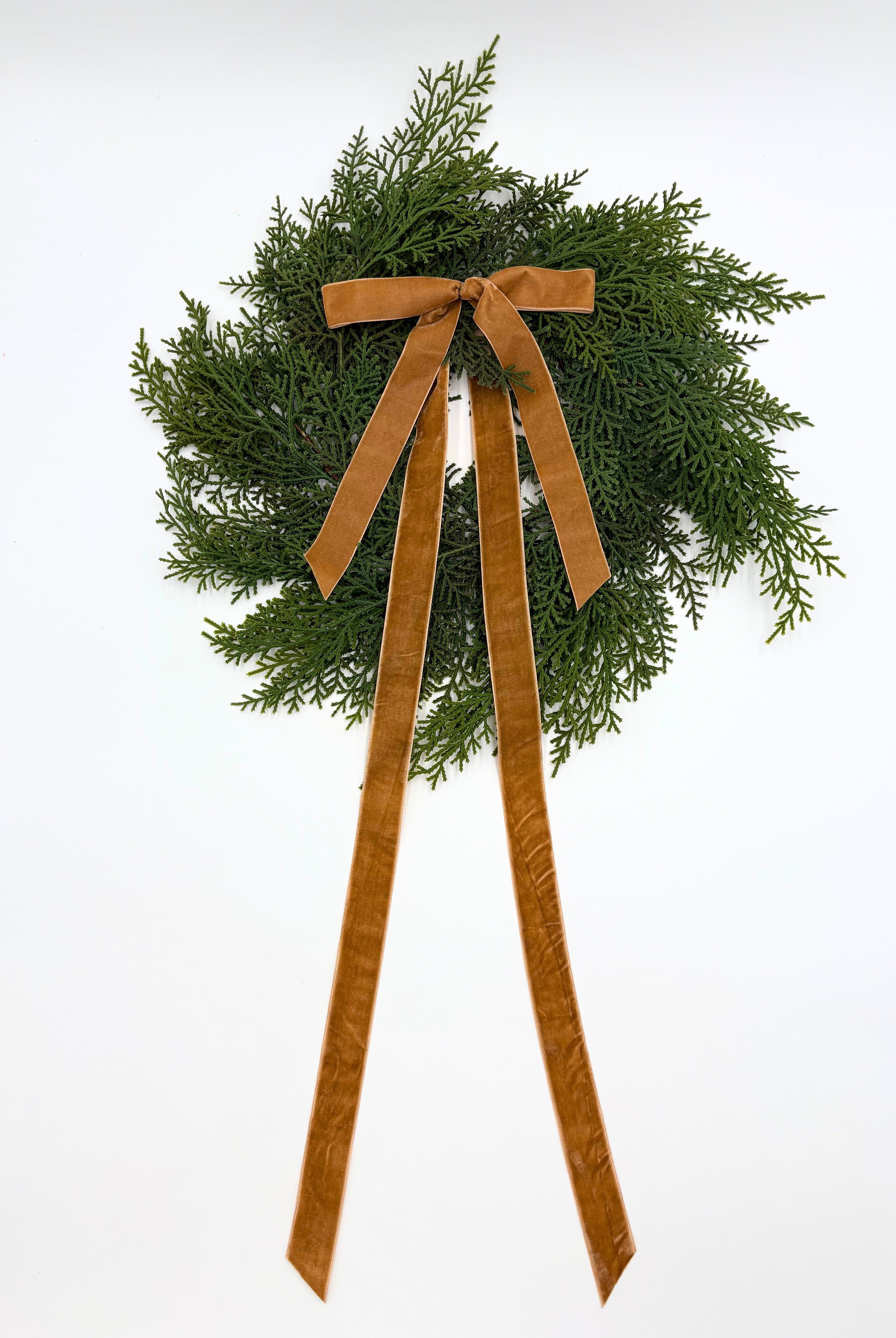 Mini faux cedar Christmas wreath featuring a long, elegant caramel velvet ribbon bow on a white background.