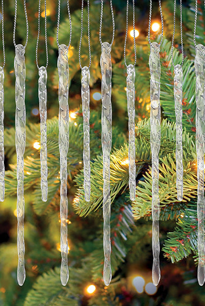 Set of 24 clear, twisted glass icicle ornaments hanging with silver strings against a lit Christmas tree.
