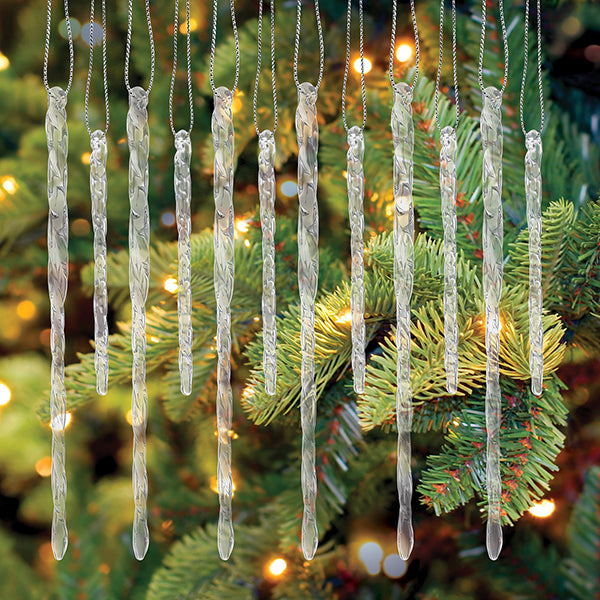 Set of 24 clear, twisted glass icicle ornaments hanging with silver strings against a lit Christmas tree.