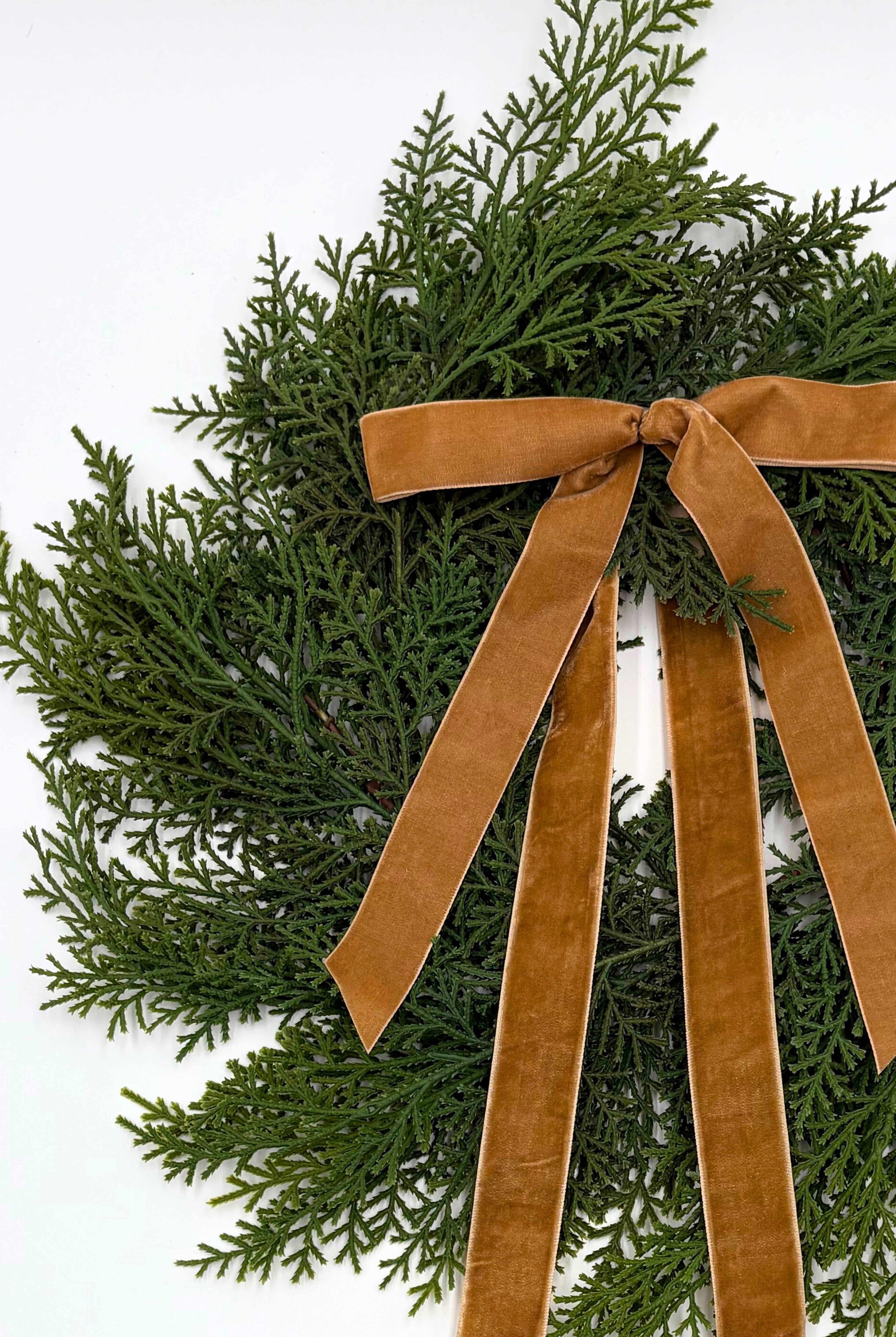 Mini faux cedar Christmas wreath accented with an elegant caramel velvet ribbon bow on a white background.
