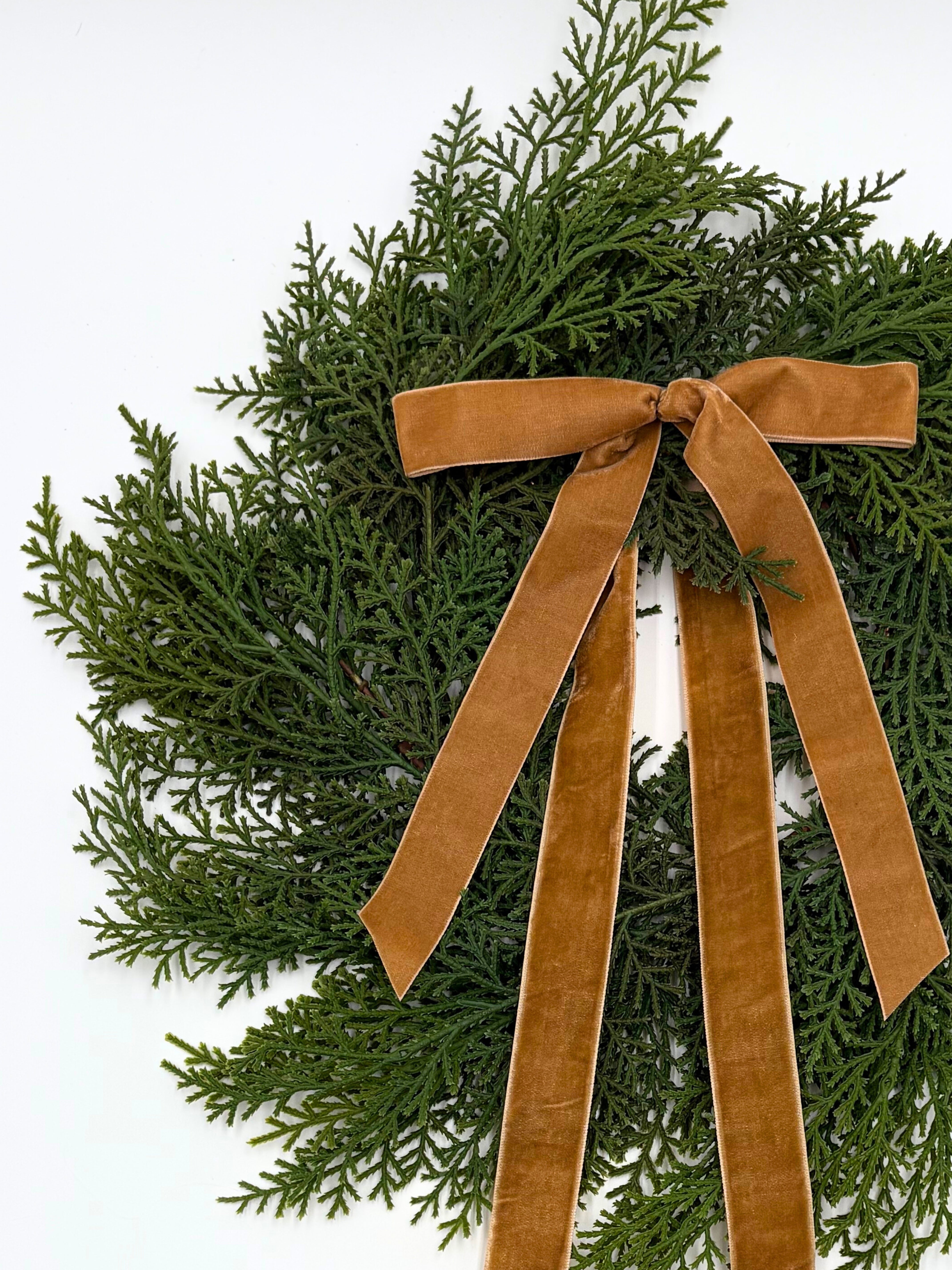 Mini faux cedar Christmas wreath accented with an elegant caramel velvet ribbon bow on a white background.