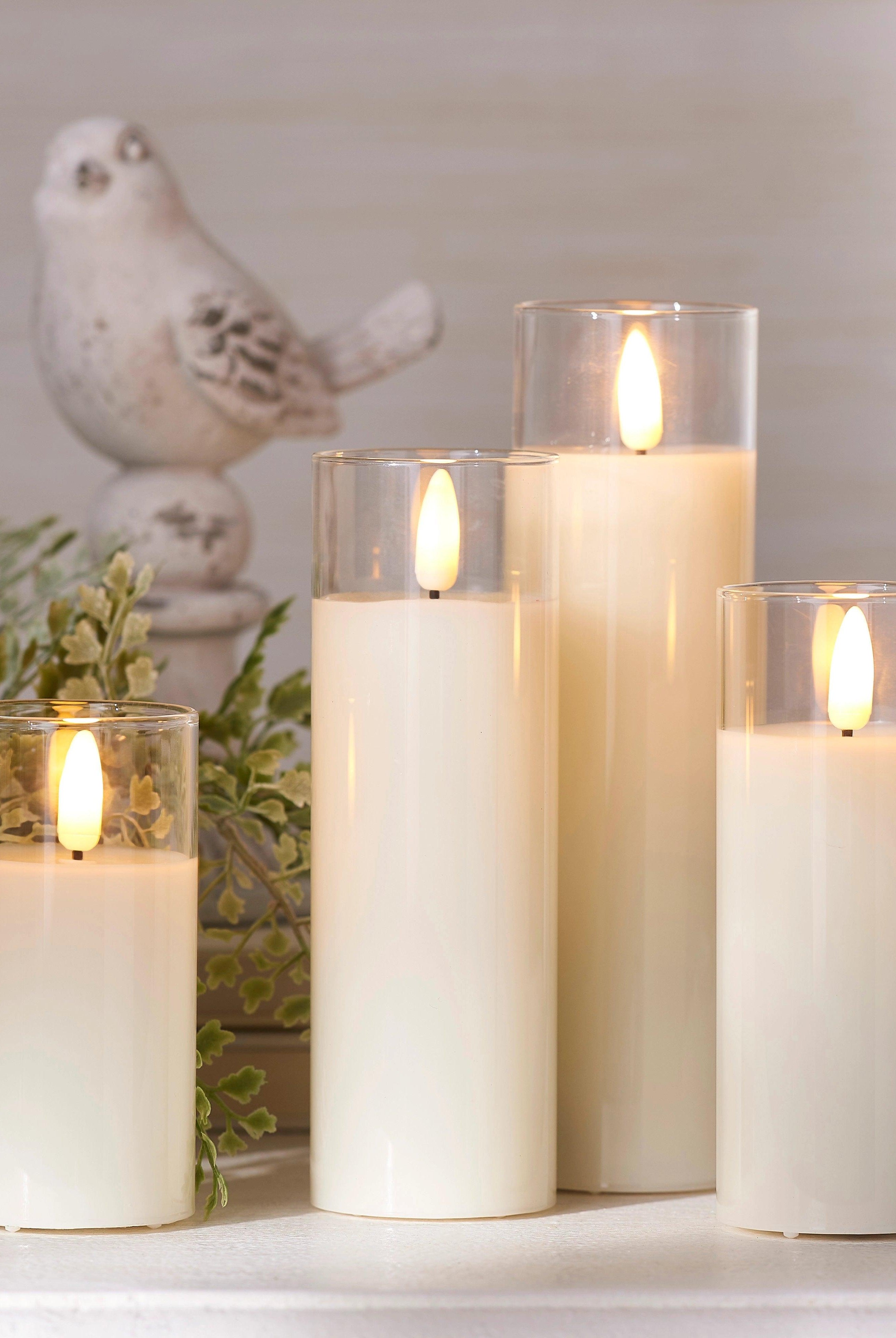 Ivory LED pillar candles in clear glass holders with realistic flickering flames, arranged on a white surface.