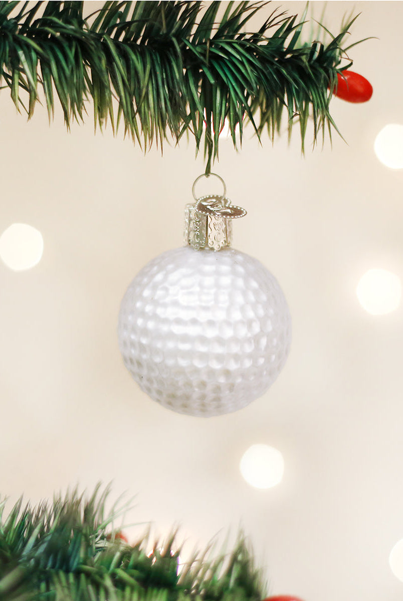 White dimpled golf ball Christmas ornament hanging from a pine branch with a silver cap against a bokeh light background.