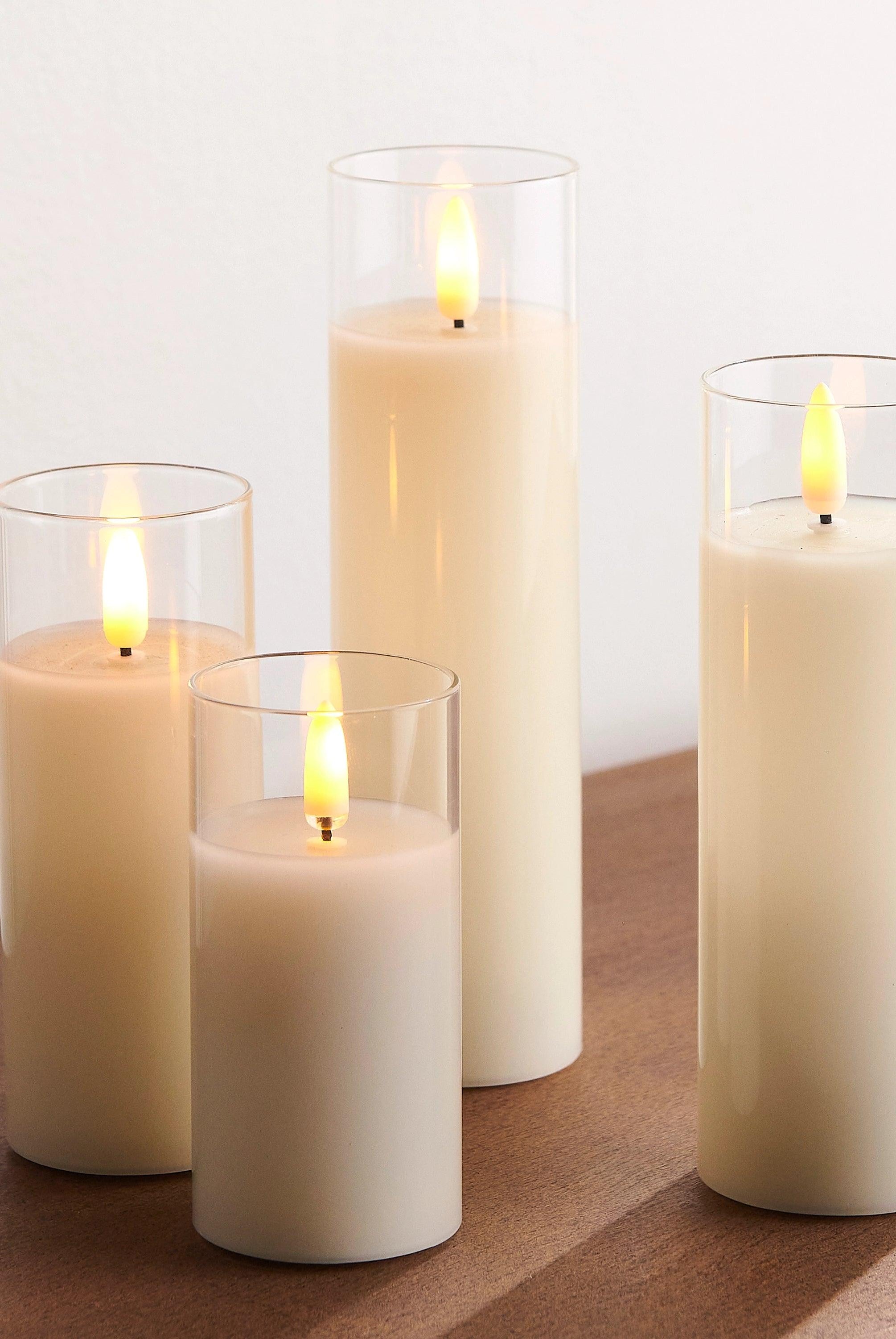 Four ivory LED pillar candles in clear glass holders with realistic flickering flames on a wooden surface.