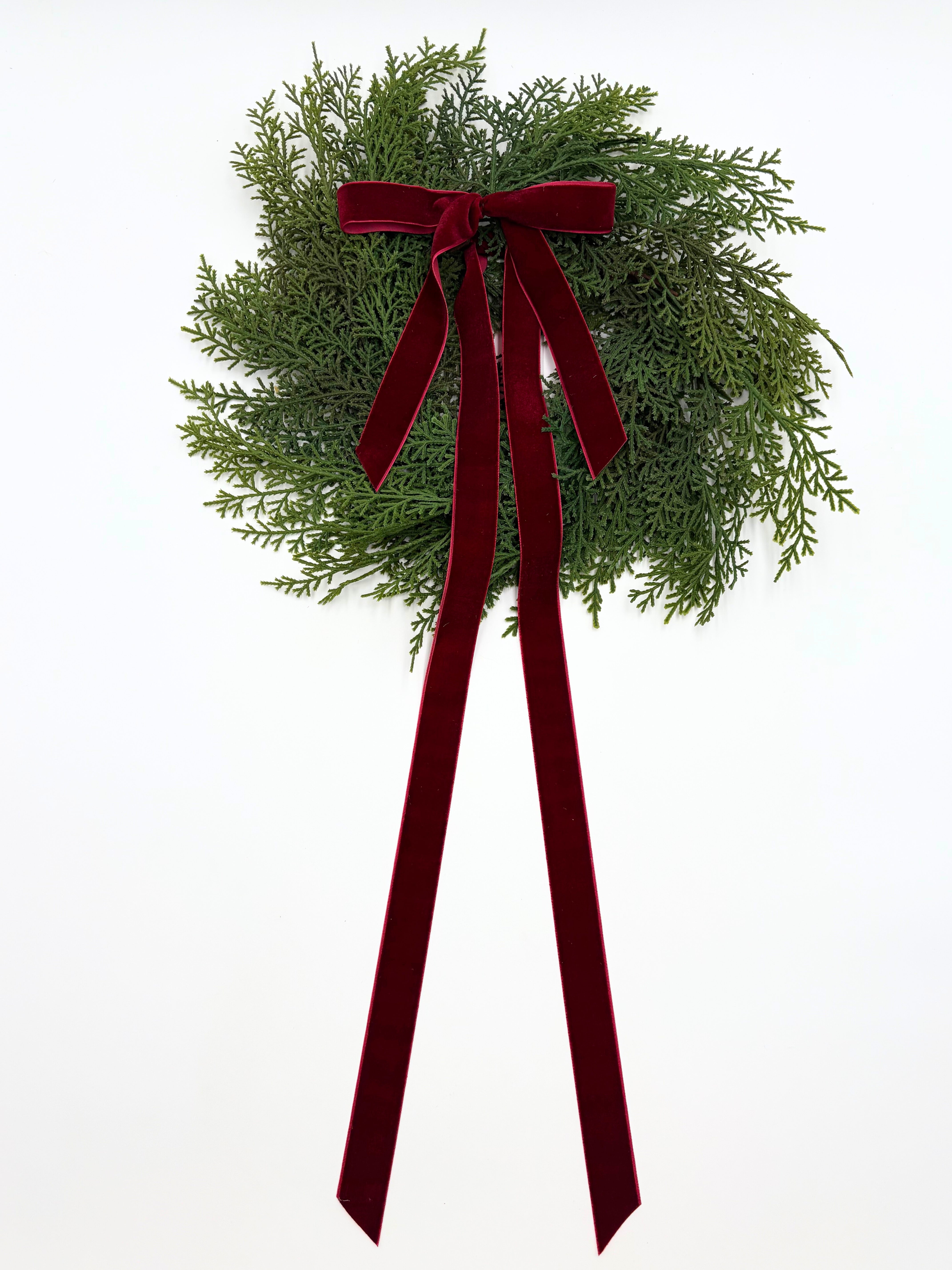 Mini faux cedar Christmas cabinet wreath featuring lush green foliage and a long, elegant deep red velvet ribbon.
