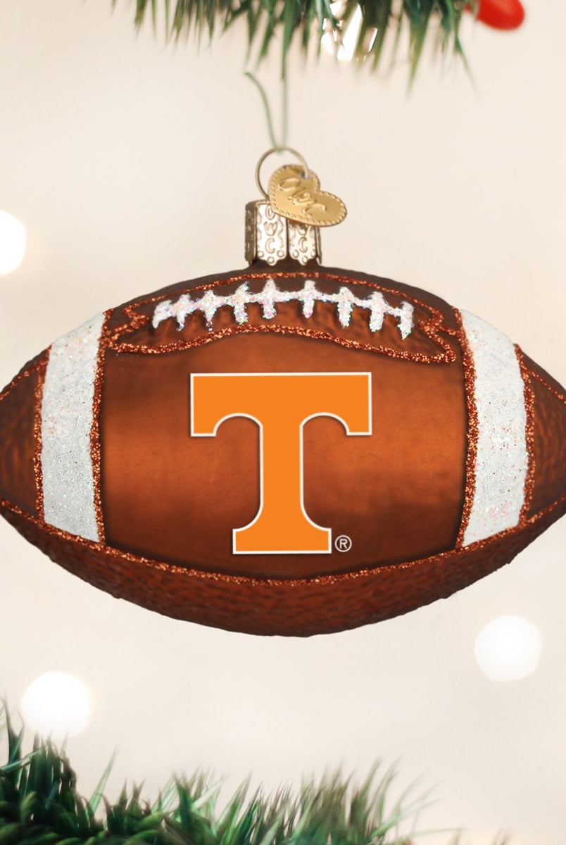 Glass Tennessee Volunteers football ornament in brown and orange with glittery white laces, hanging on a tree.