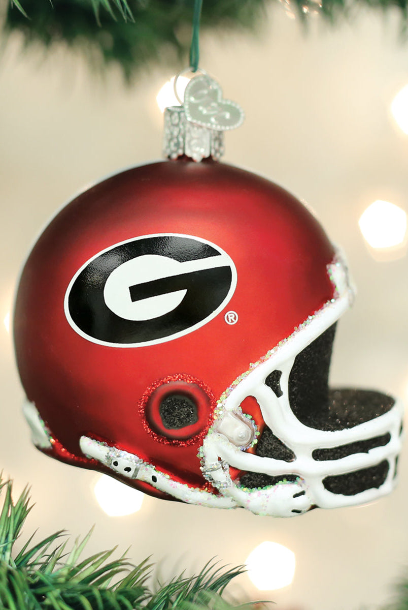 Red glass Georgia Bulldogs football helmet Christmas ornament with a white facemask and black G logo hanging on a tree.