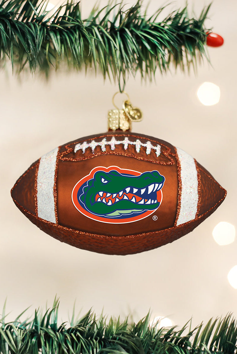 Brown glass football ornament featuring the Florida Gators logo, white glitter laces, and hanging on a pine branch.
