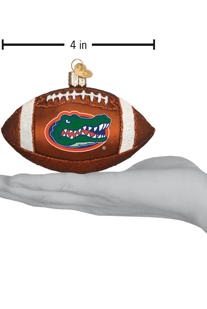 4-inch brown glass Florida Gators football ornament with white laces and team logo, held in a hand.