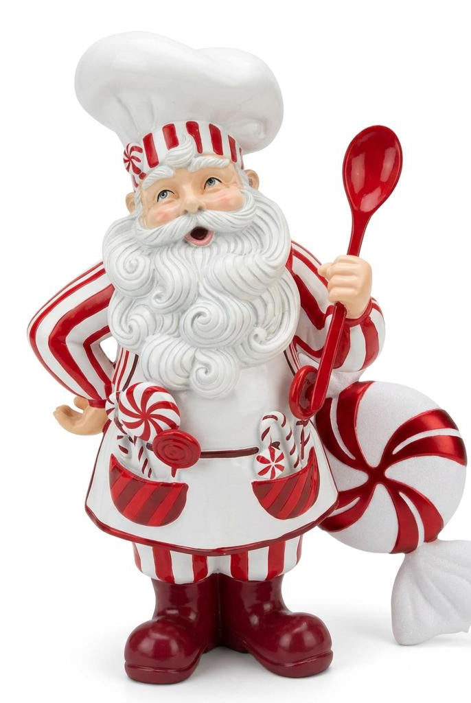 Front view of glossy resin Santa chef holding red spoon beside giant candy cane decoration