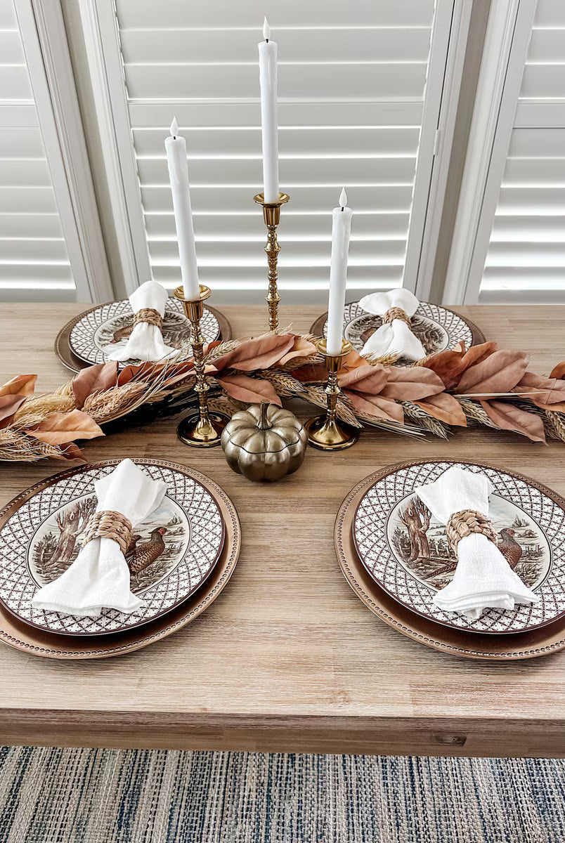 72-inch wheat and dried leaf garland centerpiece on a rustic dining table with brass candlesticks and autumn place settings.