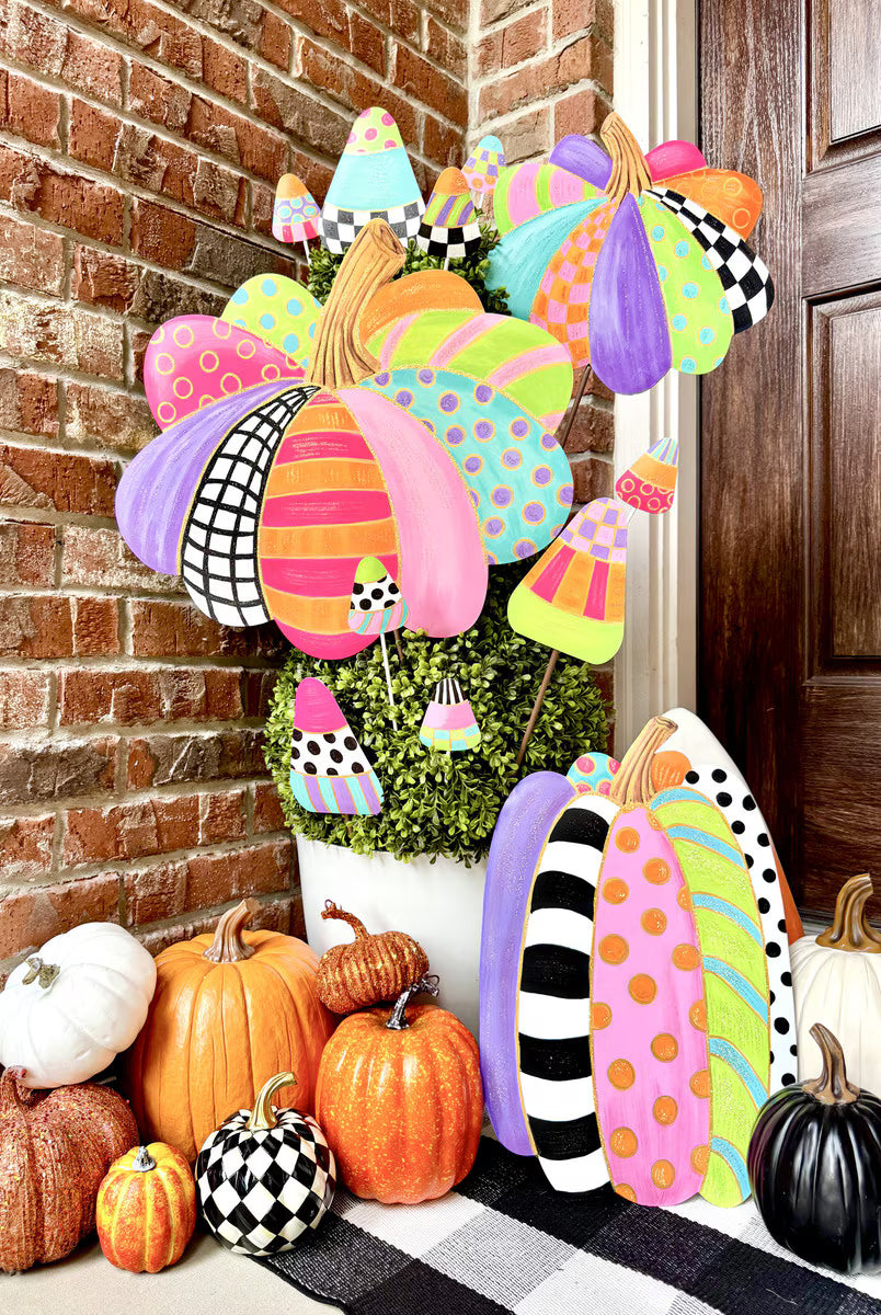 Colorful patterned pumpkin stakes with polka dots and stripes, displayed in a planter with assorted decorative pumpkins.
