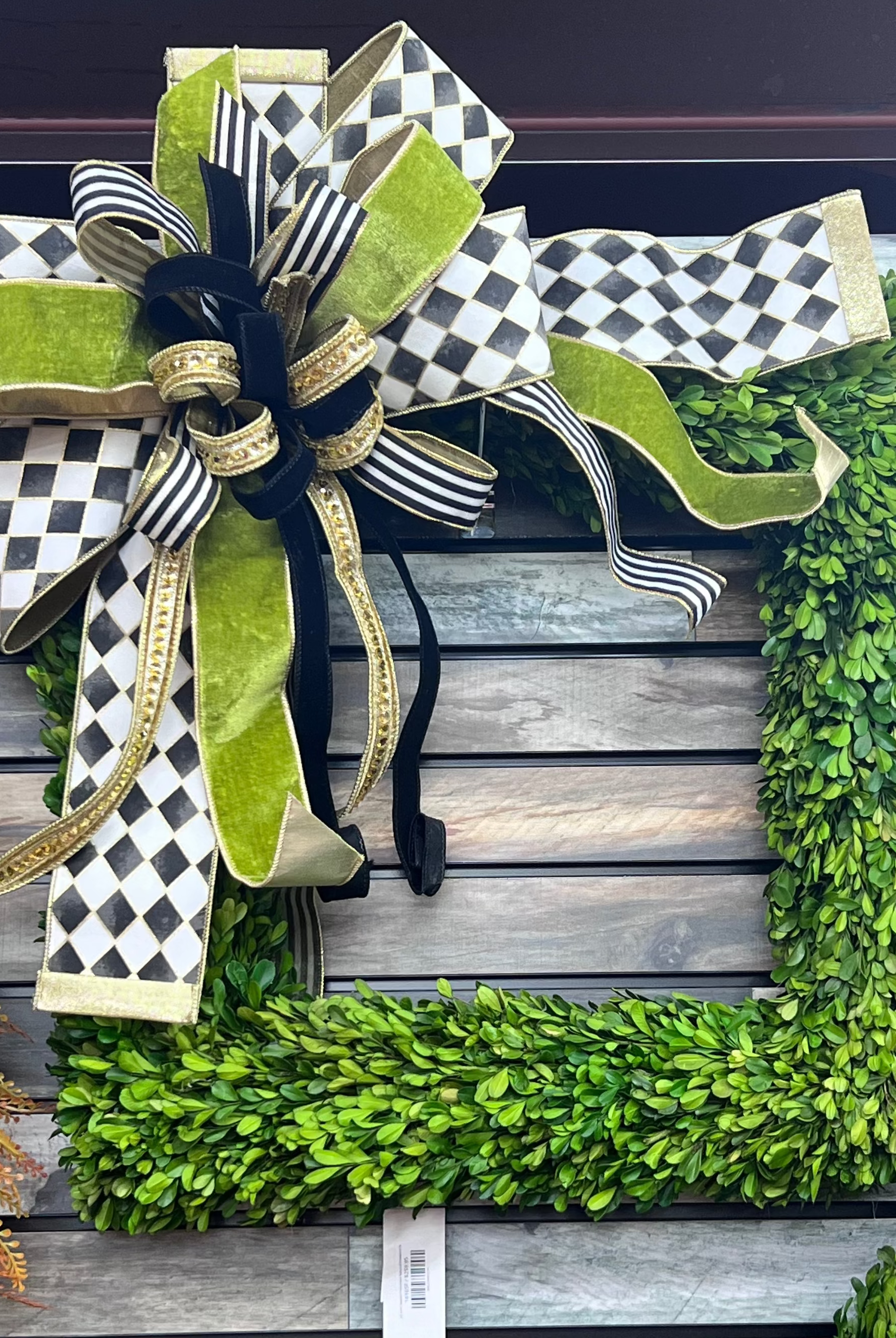 Large decorative bow featuring black and white checkered ribbon, lime green velvet, and gold accents on a boxwood wreath.