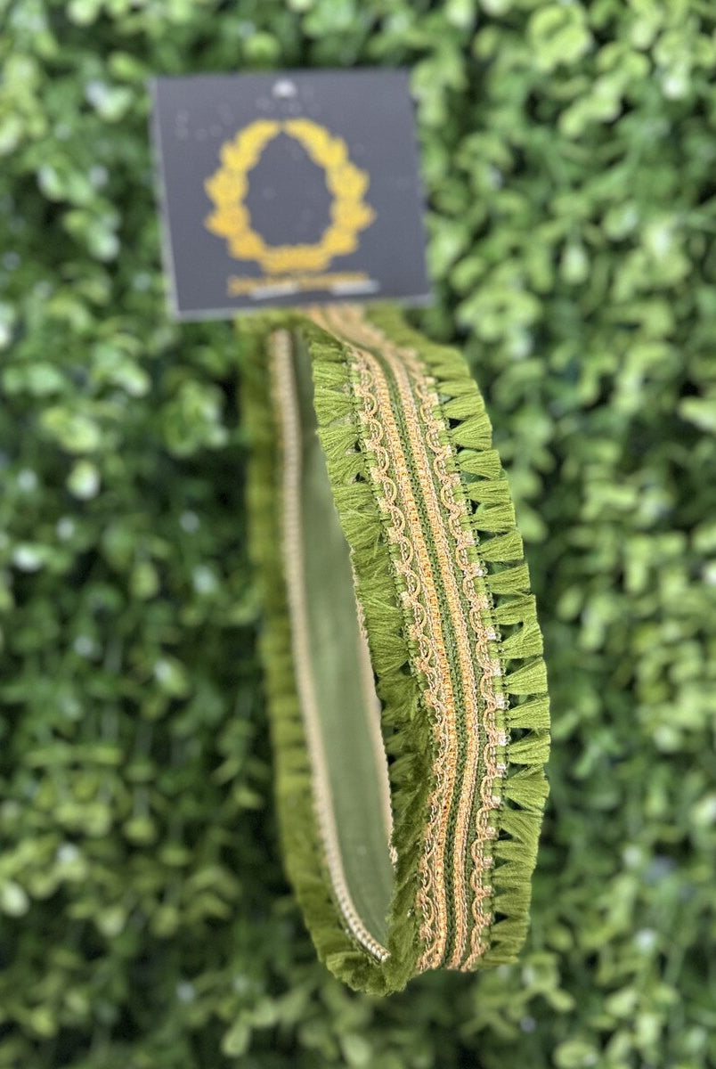 Olive green JME ribbon with fringed edges and decorative gold trim, displayed against a green faux boxwood background.