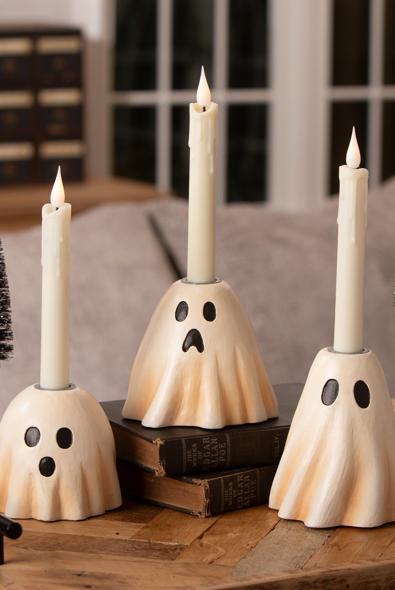 Three vintage-style cream resin ghost candlesticks with black eyes and mouths, each holding a white taper candle.