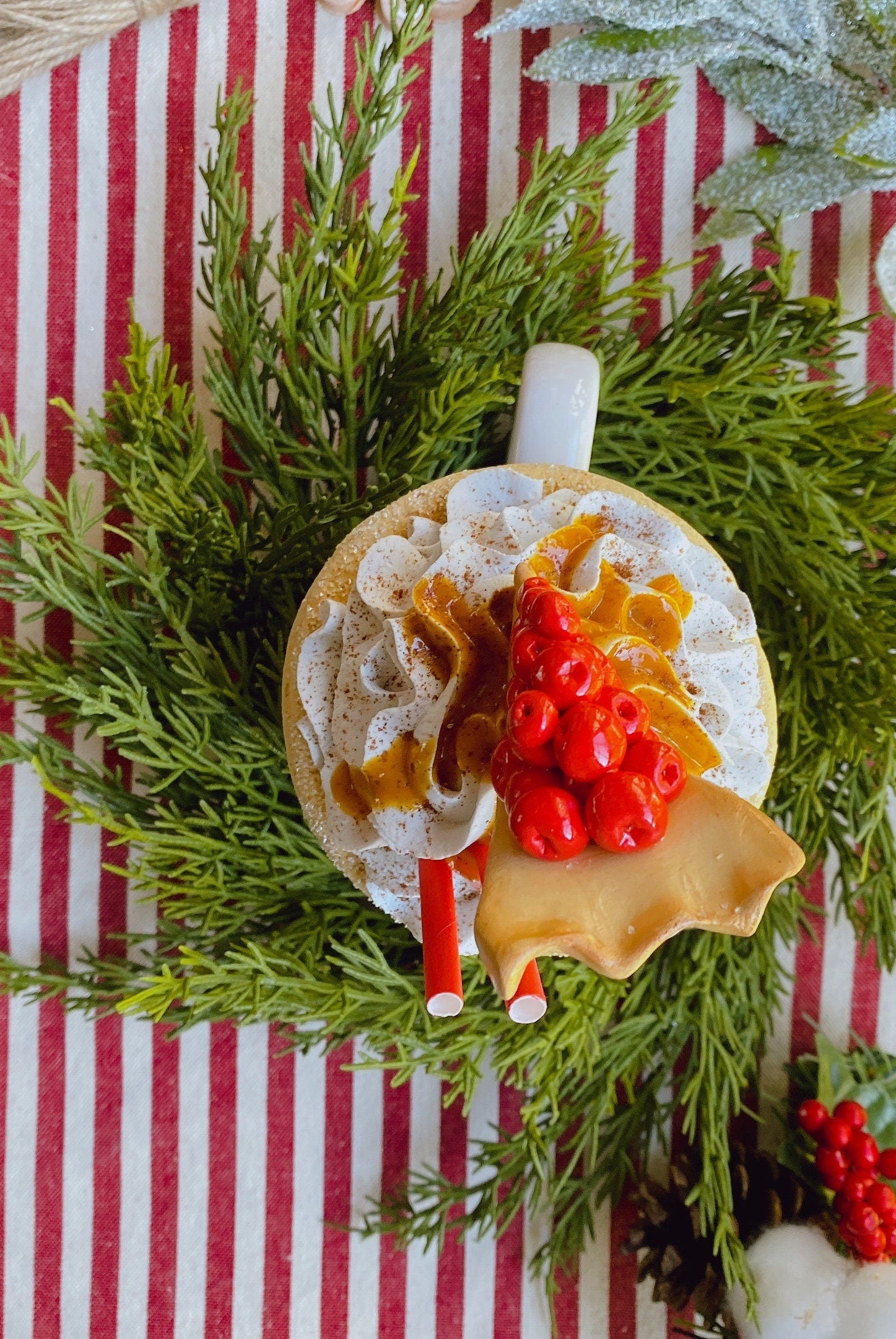 14-inch faux cedar mini Christmas wreath surrounding a festive mug on a red and white striped table runner.