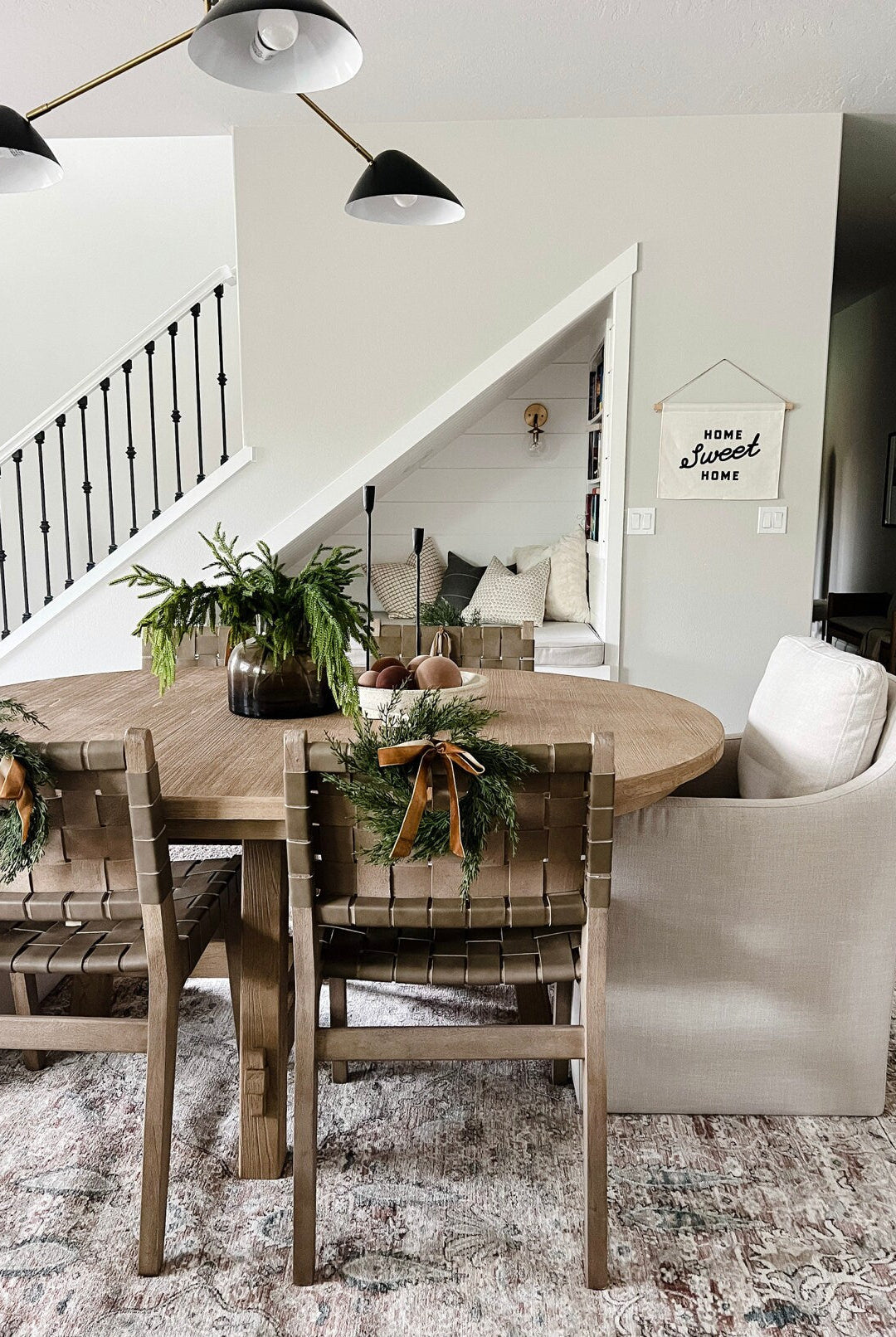 Mini faux cedar wreaths with caramel velvet ribbons hanging on wooden dining chairs in a farmhouse-style dining room.