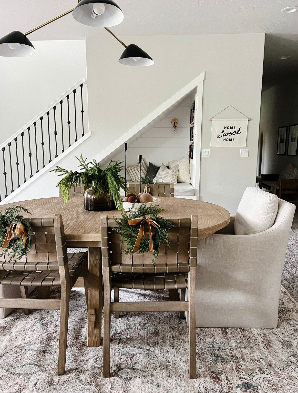 Mini faux cedar wreaths with caramel velvet ribbons hanging on wooden dining chairs in a farmhouse-style dining room.