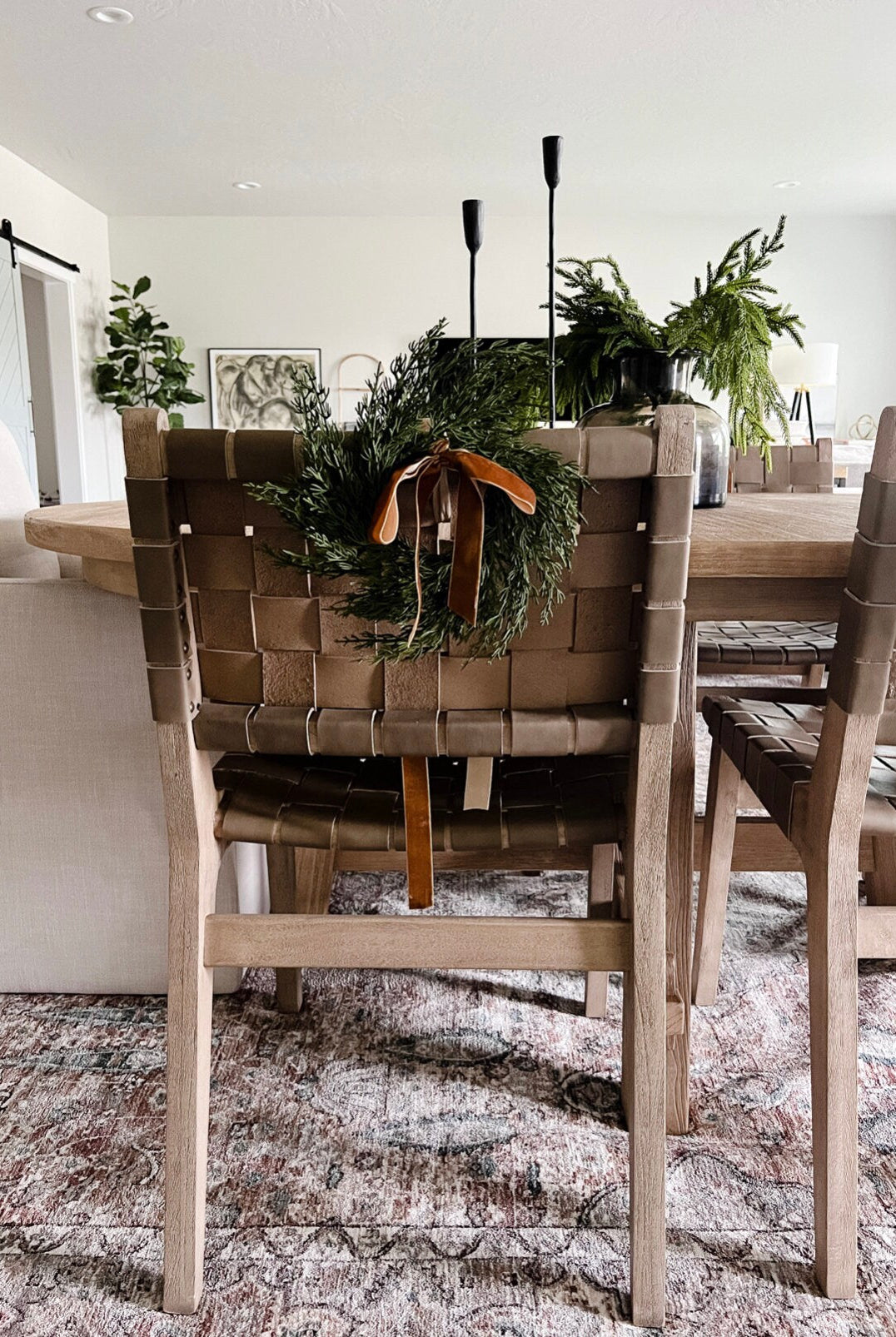 Mini faux cedar wreath with a caramel velvet ribbon hanging on the back of a woven leather dining chair.