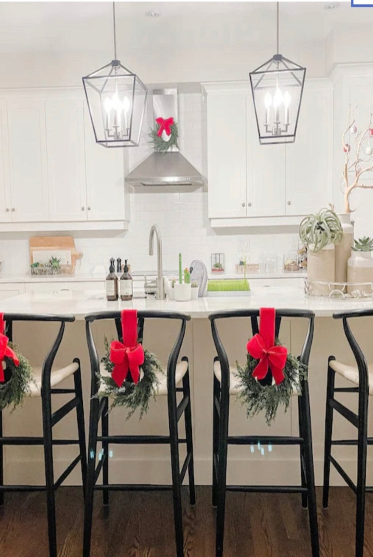 Mini artificial cedar Christmas wreaths with bright red bows hanging on black kitchen bar stools and cabinets.