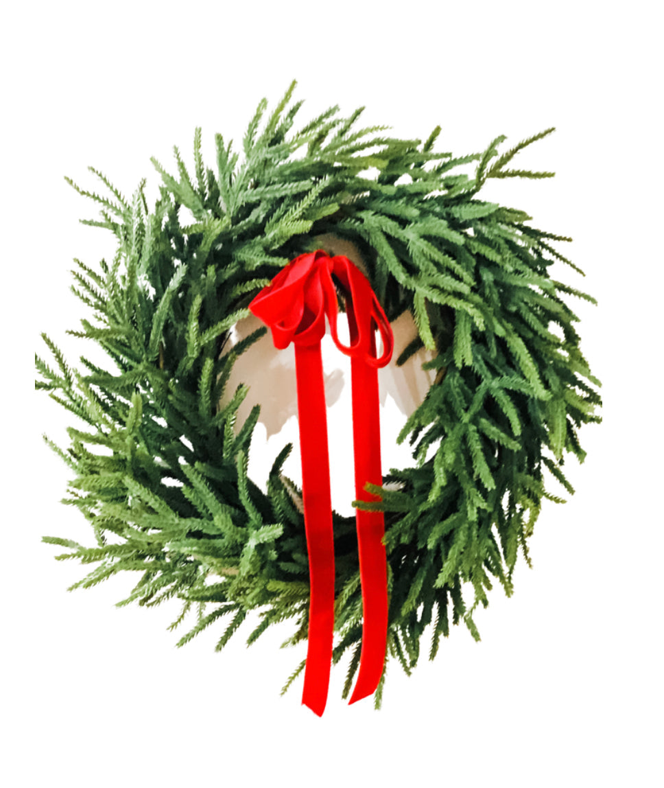 Lifelike Norfolk pine winter wreath with lush green needles and a festive red velvet ribbon bow.