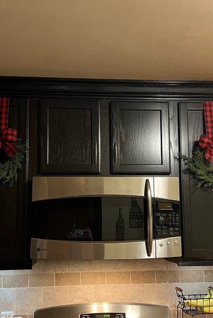 Mini artificial cedar Christmas wreaths with red and black buffalo plaid ribbon hanging on dark kitchen cabinets.