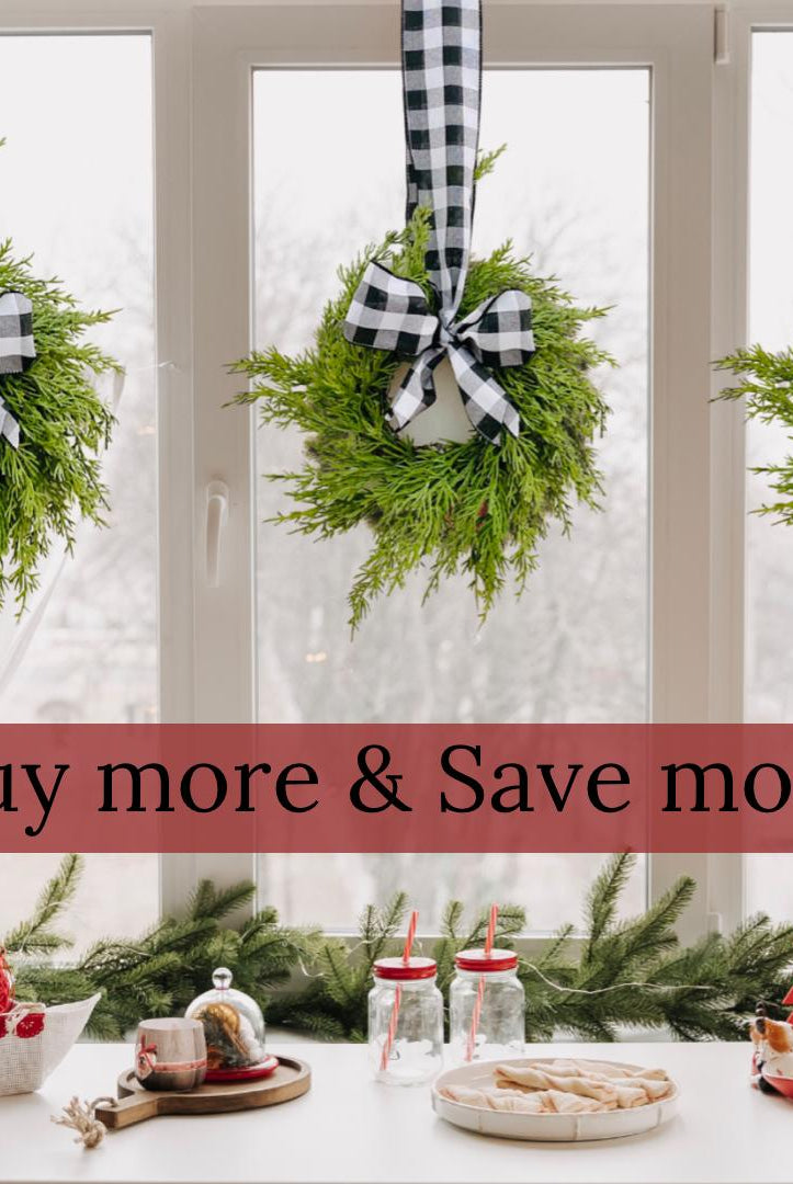 Three mini artificial cedar wreaths hanging on a window with black and white buffalo check ribbons and bows.