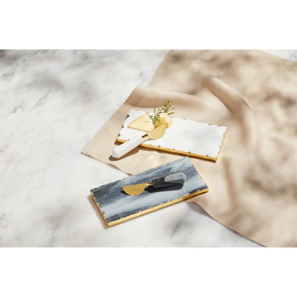 Gray and white marble serving boards with gold foil raw edges and matching marble-handled brass spreaders.
