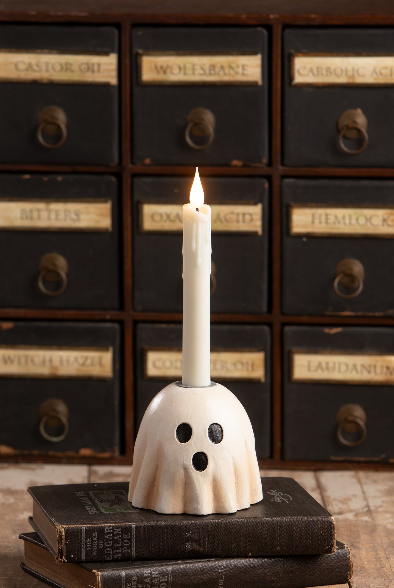 Bethany Lowe hand-painted resin surprised ghost candlestick holding a white taper candle on vintage books.