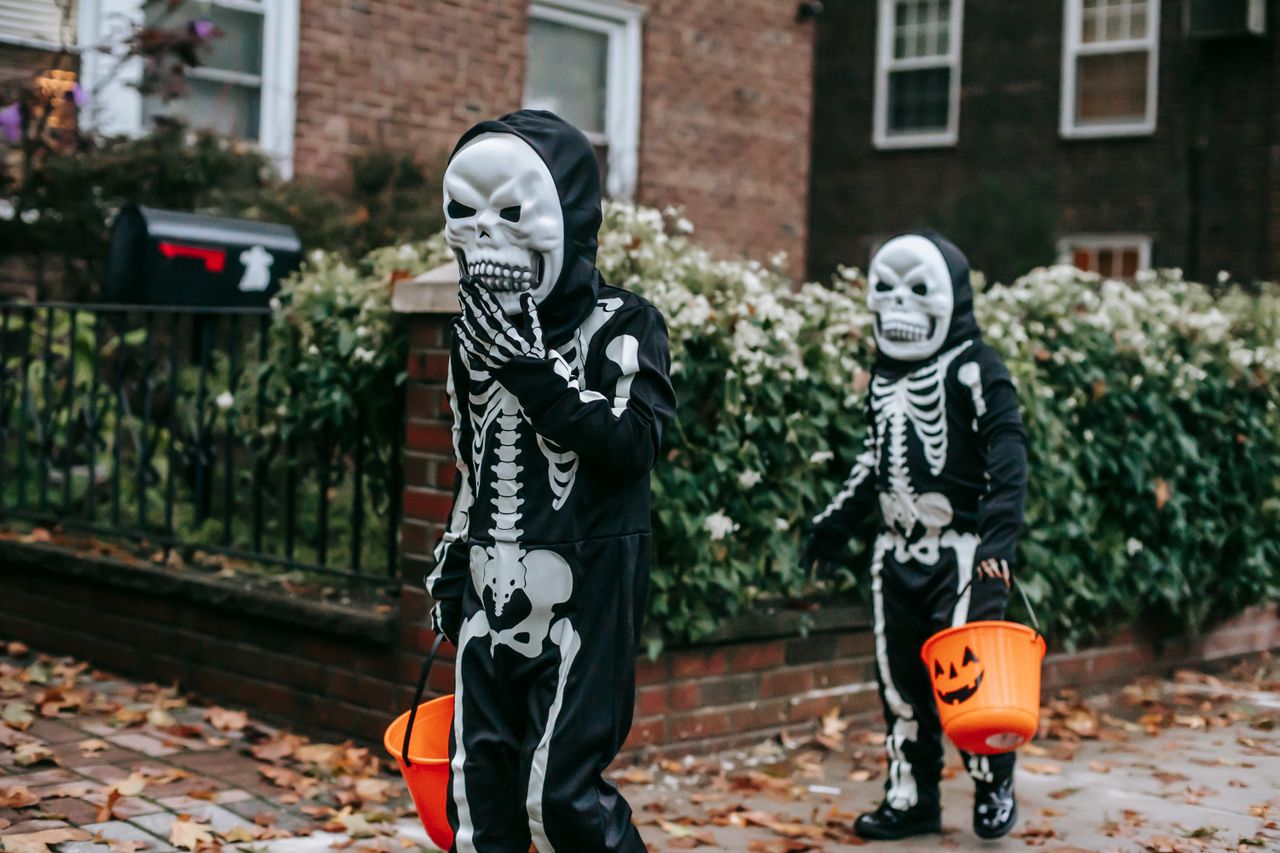 Two children in skeleton costumes trick-or-treating with buckets. 