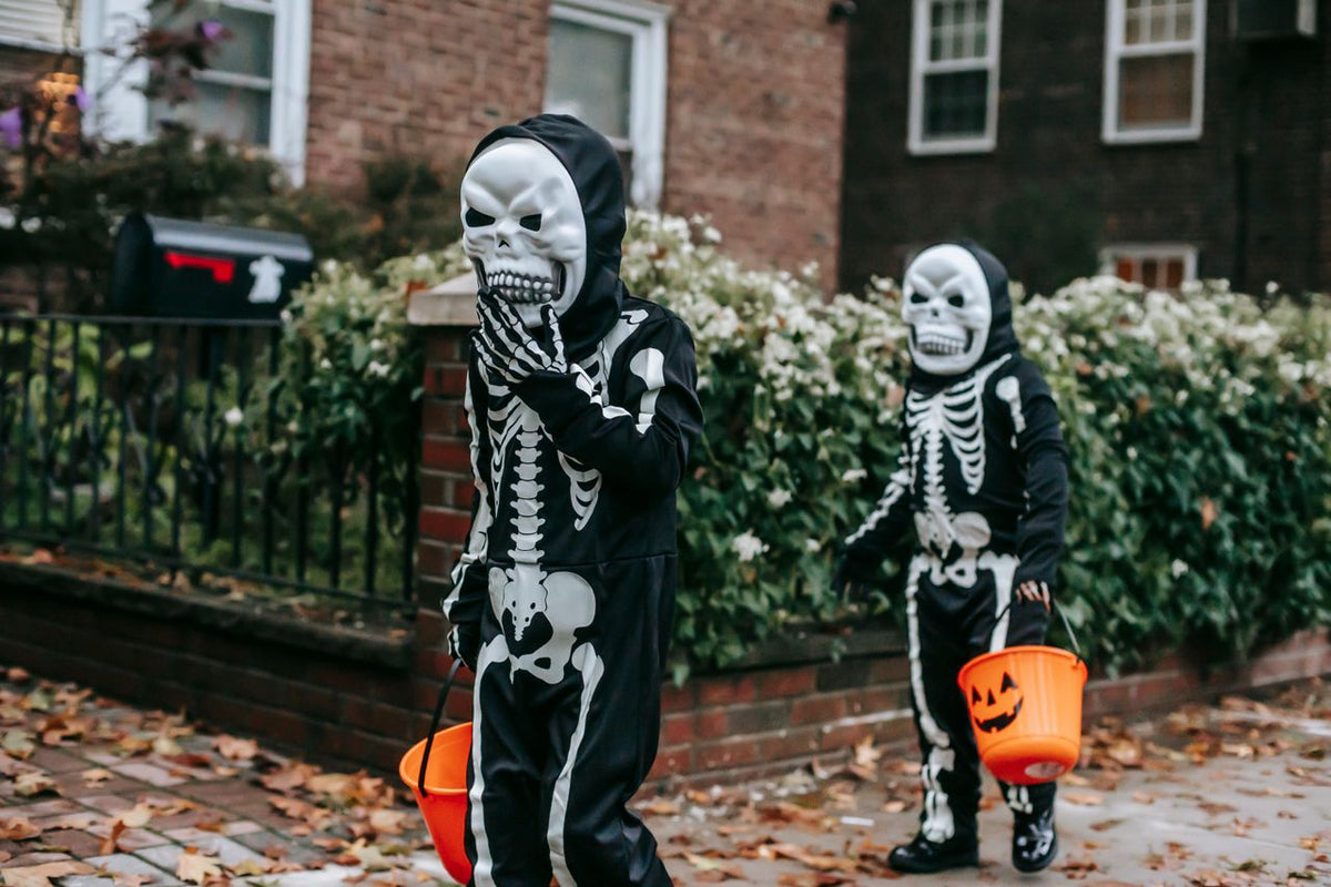 Two children in skeleton costumes trick-or-treating with buckets. 