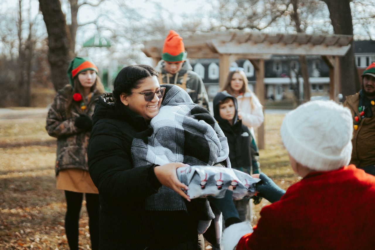 Smiling woman receives wrapped gift outdoors.