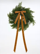 Mini faux cedar Christmas wreath featuring a long, elegant caramel velvet ribbon bow on a white background.