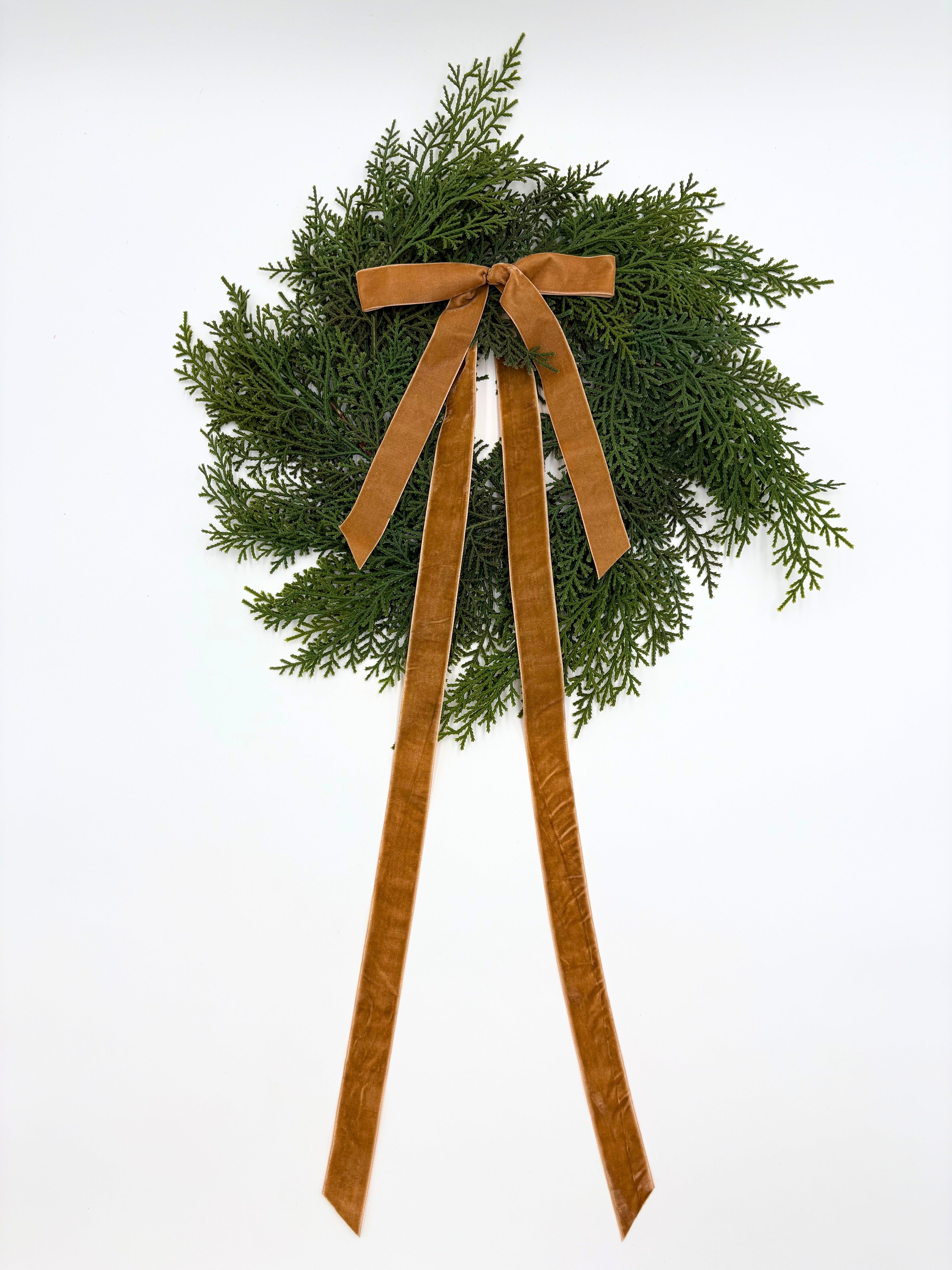 Mini faux cedar Christmas wreath featuring a long, elegant caramel velvet ribbon bow on a white background.
