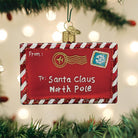 Red glass ornament shaped like a letter to Santa with white and red striped borders, gold postmark, and snowflake stamp.