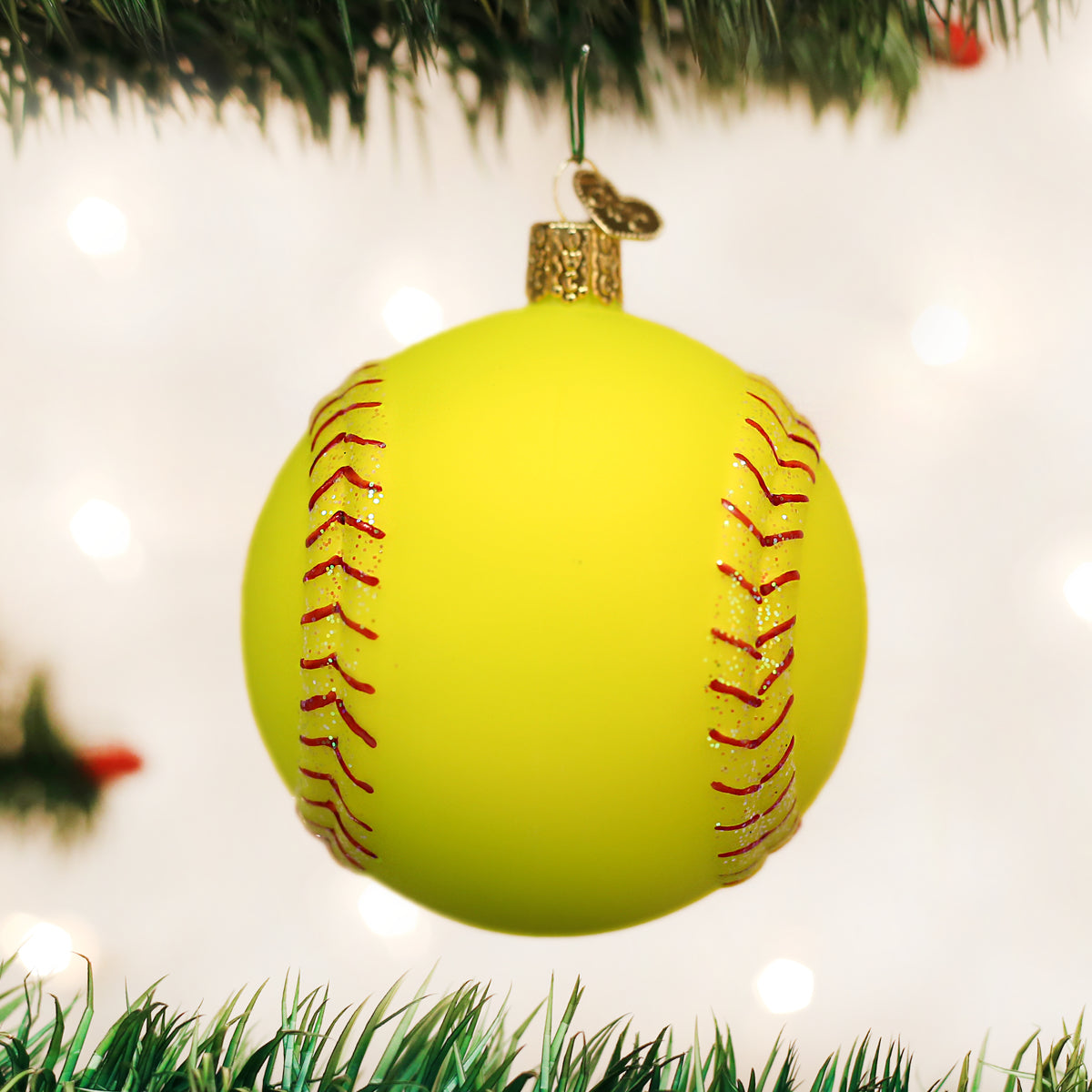 Bright yellow glass softball Christmas ornament with red glitter stitching hanging from a tree branch.