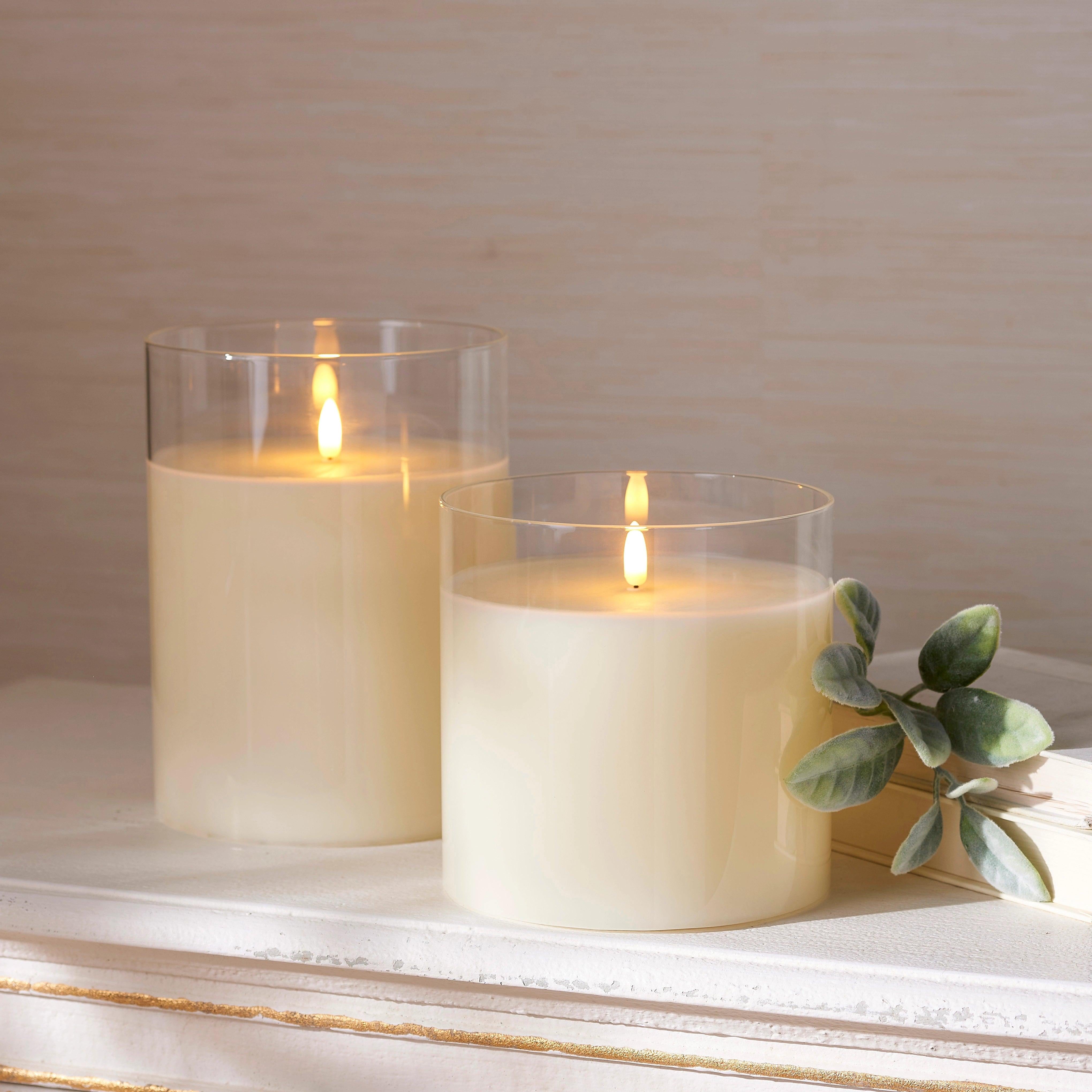 Two 6-inch ivory LED pillar candles in clear glass holders with realistic flickering flames on a white mantel.
