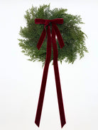 Mini faux cedar Christmas cabinet wreath featuring lush green foliage and a long, elegant deep red velvet ribbon.