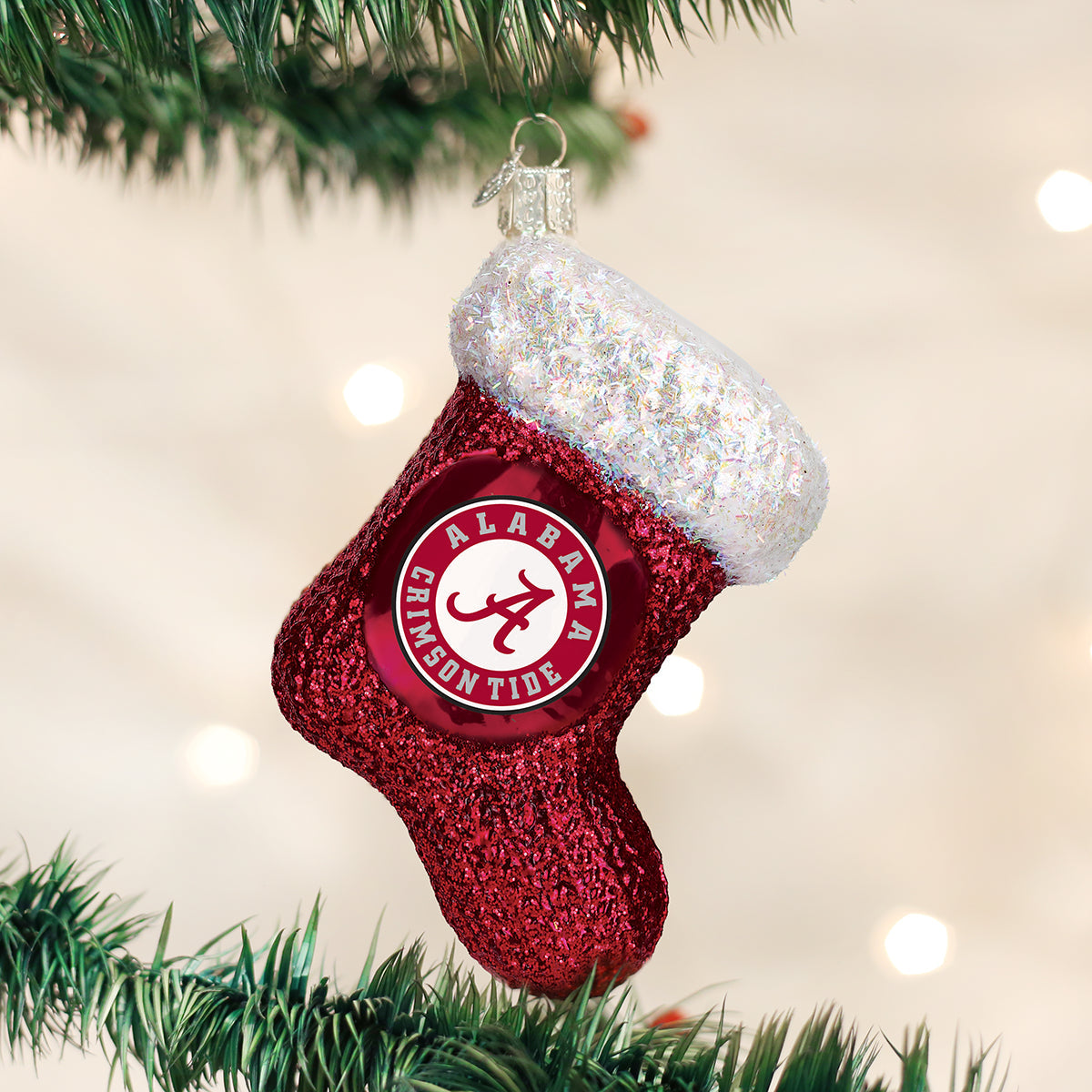 Red glittery Alabama Crimson Tide stocking ornament with a white iridescent cuff hanging on a Christmas tree.