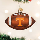 Glass Tennessee Volunteers football ornament in brown and orange with glittery white laces, hanging on a tree.