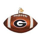 Brown glass football ornament featuring the Georgia Bulldogs G logo, white glitter accents, and a gold heart charm.