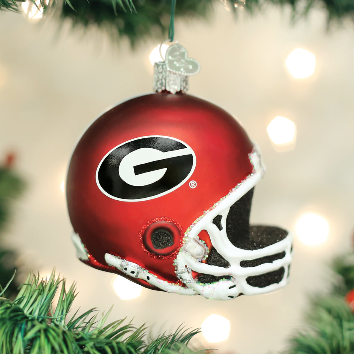 Red glass Georgia Bulldogs football helmet Christmas ornament with a white facemask and black G logo hanging on a tree.