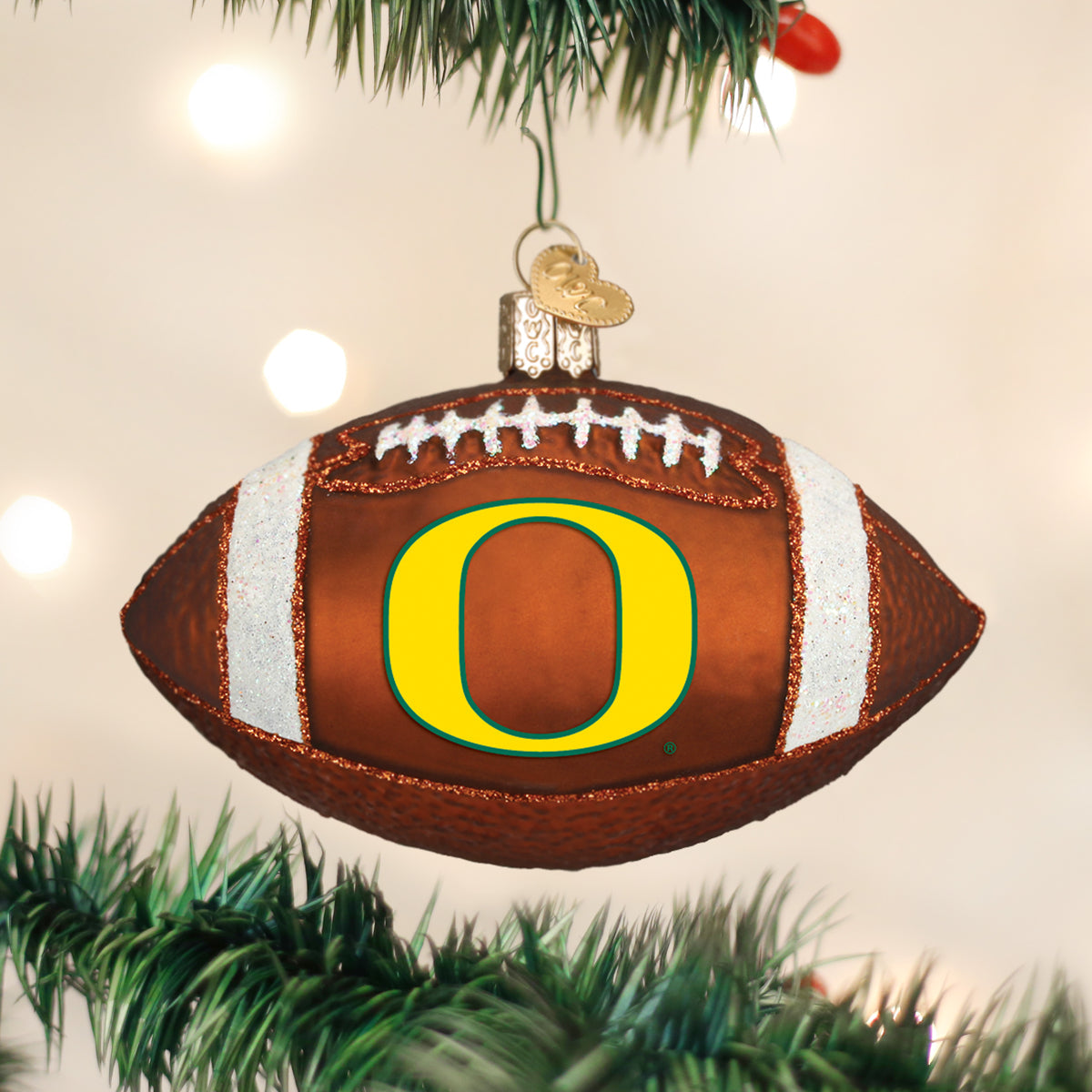 Glass Oregon Ducks football ornament featuring a yellow O logo, white glitter stripes, and a gold heart charm.