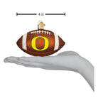 4-inch brown glass Oregon Ducks football ornament with white laces and a yellow O logo held in a hand.